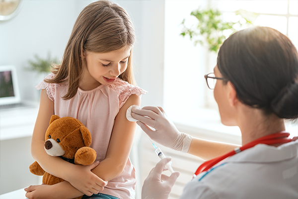 A girl holding onto a teddy bear while getting her shot.