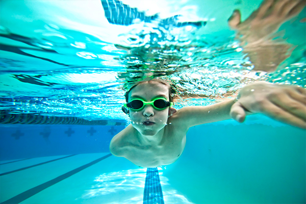 A boy swimming in the pool with goggles on.